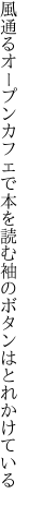 風通るオープンカフェで本を読む 袖のボタンはとれかけている