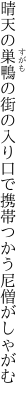 晴天の巣鴨の街の入り口で 携帯つかう尼僧がしゃがむ