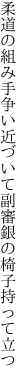 柔道の組み手争い近づいて 副審銀の椅子持って立つ